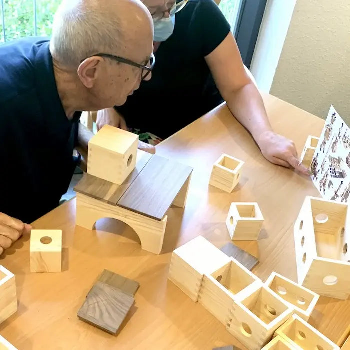Ein ältere Herr baut gemeinsam mit eine Betreuerin ein Baumuster nach. Der ältere Mann schaut konzentriert auf die Bauanleitung.