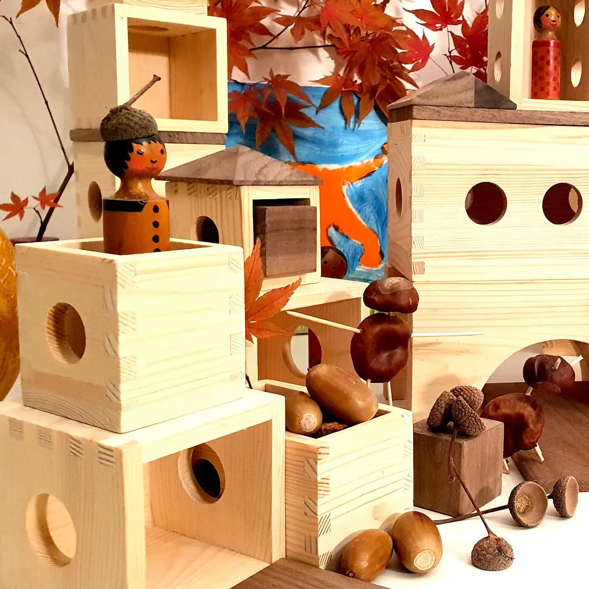 Nahaufnahme einer herbstliche Szene mit Matzbox-Bausteinen. In einer Kiste liegen Eicheln. In einer Box steht eine Figur eine Kastanientier läuft durch ein Tor