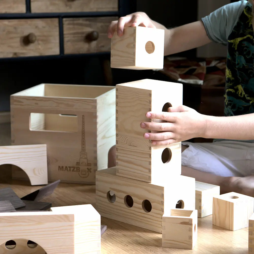 Bild von Matzbox Bausteinen auf dem noch die Hände eines kindes zu sehen sind das sie gerade gefühlvoll aufeinander stapelt um etwas schönes zu bauen