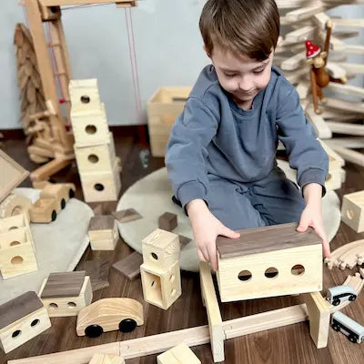 Ein junge stzt im Kinderzimmer und spielt mit der Matzbox. Erbaut eine Landschaft für seine Holzeisenbahn